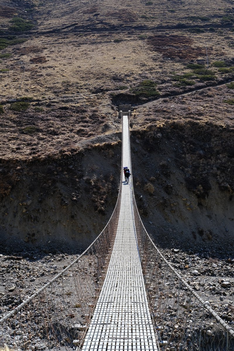 The porters cross a bridge in the barren landscape